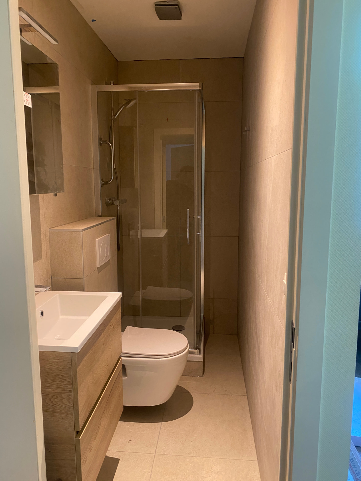 Afgewerkte badkamer met beige tegels, houten wastafelmeubel en glazen douchecabine