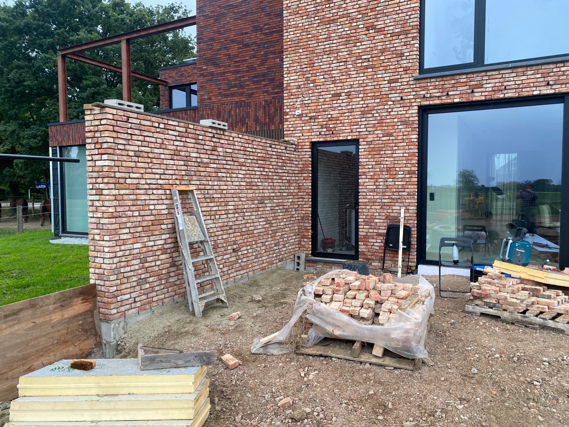 Bijna afgewerkte bakstenen buitenmuur met ladder en materiaal op de werf